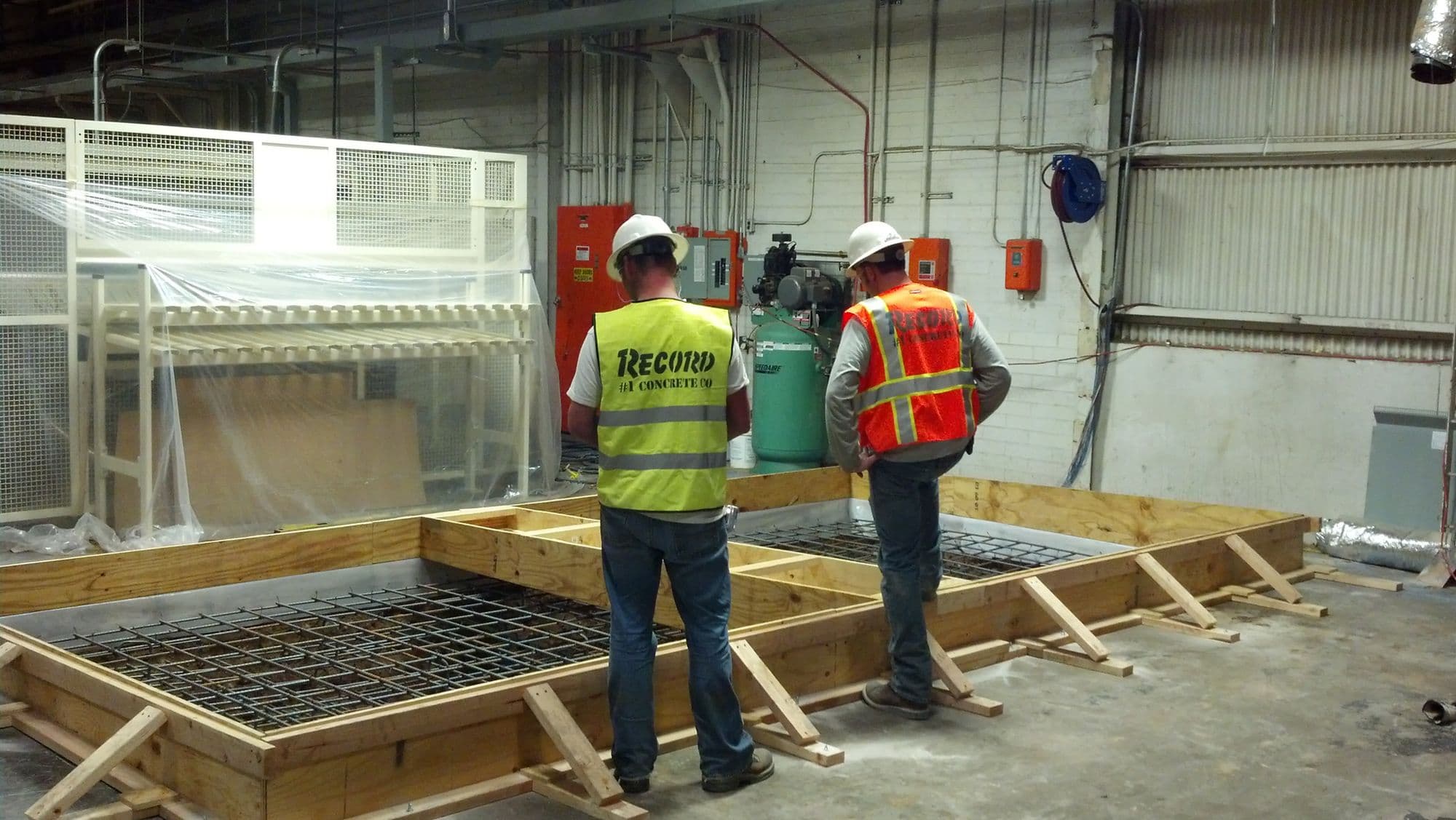Two workers in Record Construction hi-vis vests forming and setting rebar